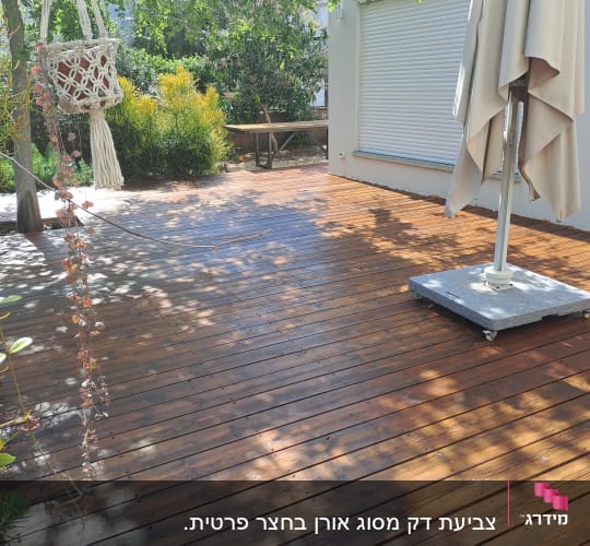 דק עץ עם שמשיה ועציץ תלוי בגינה